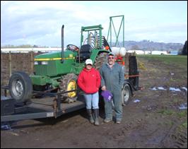 Two people pose in front of tractor loaded on a flatbed trailer.