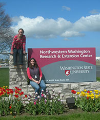 Two graduate students sit on the WSU NWREC sign.