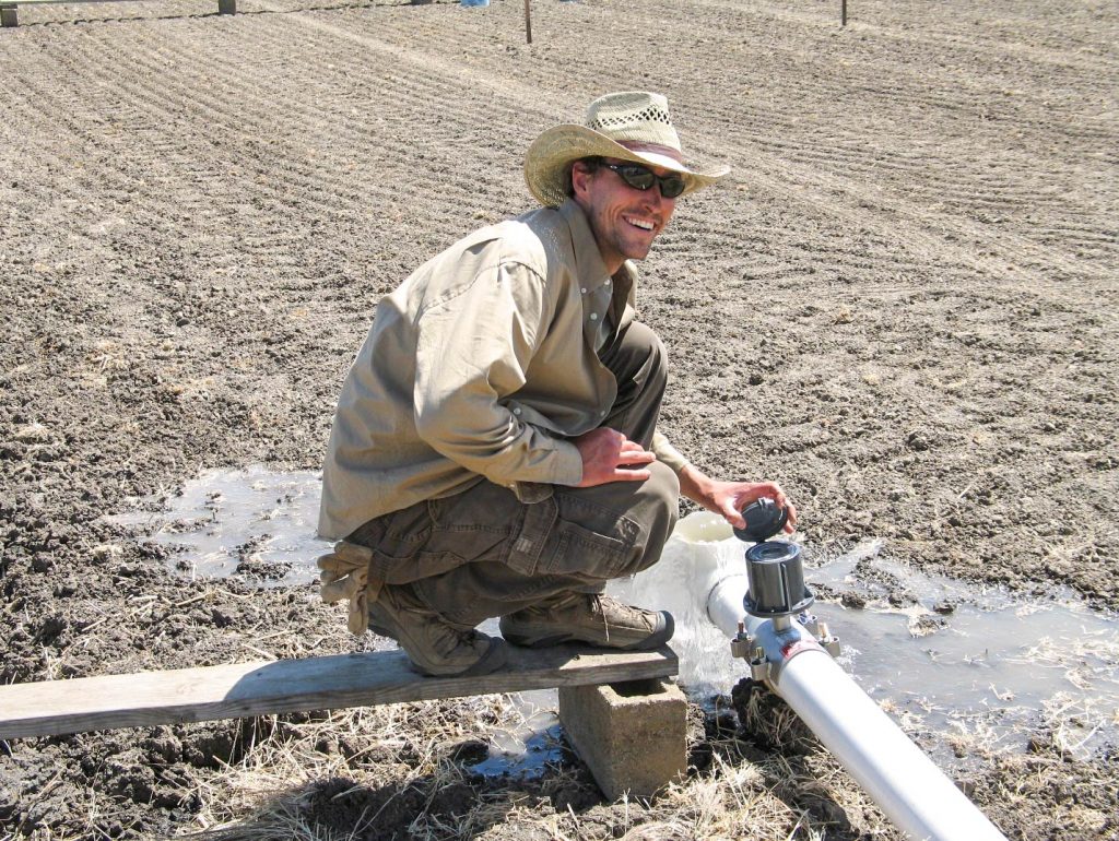 Gabe LaHue crouches to check an irrigation line in a plowed field.